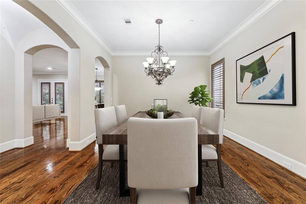 The formal dining room features an ornate wrought-iron chandelier, rich hardwood floors, and arched openings that lead to the dry bar, creating an elegant setting for hosting gatherings or intimate dinners. This photo has been virtually staged.