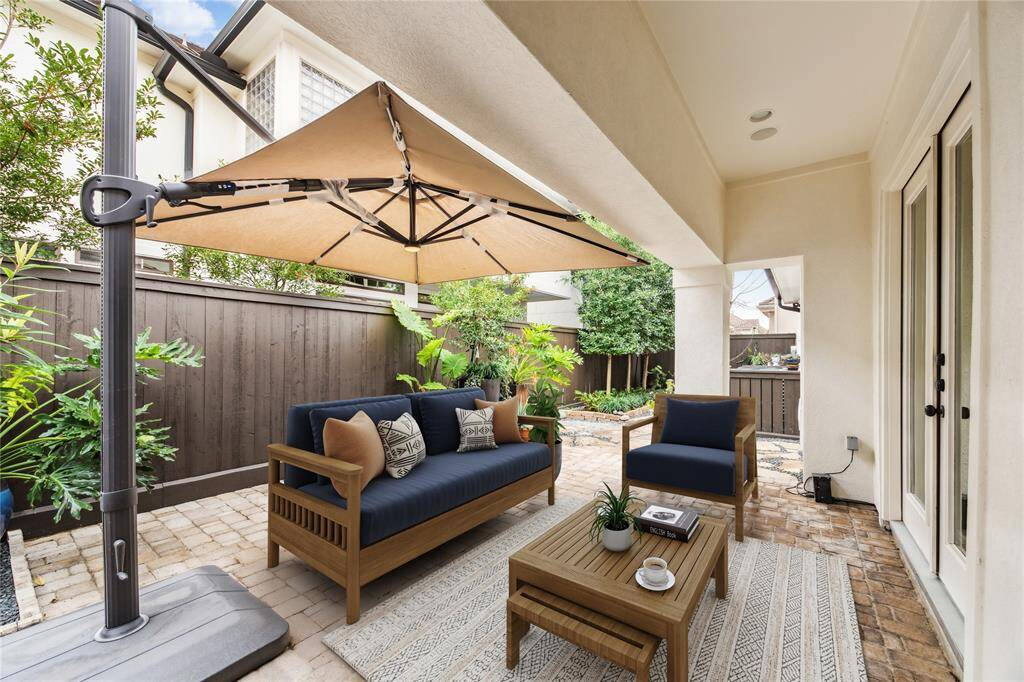 The private backyard features a covered patio with concrete pavers, an oversized cantilever umbrella, and lush professional landscaping. A stone pathway with flagstone slabs and crushed granite inlay adds character to the serene outdoor space. This photo has been virtually staged.