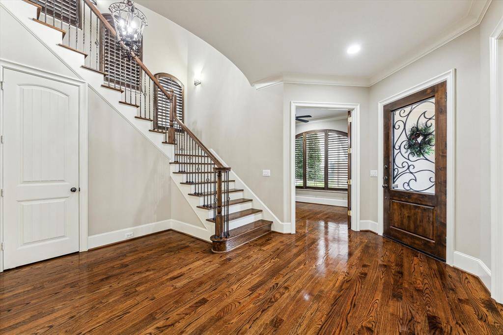 Another view of the grand foyer highlights its rich hardwood floors, soaring ceilings, and elegant staircase with wood treads and decorative iron railings. This welcoming space provides access to the half bath, a walk-in storage closet tucked beneath the staircase, and the elevator closet.