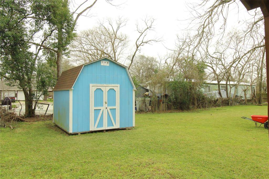 This photo showcases a spacious backyard with a vibrant blue storage shed. The yard is grassy and open, featuring a few mature trees , offering ample space for outdoor activities or gardening.