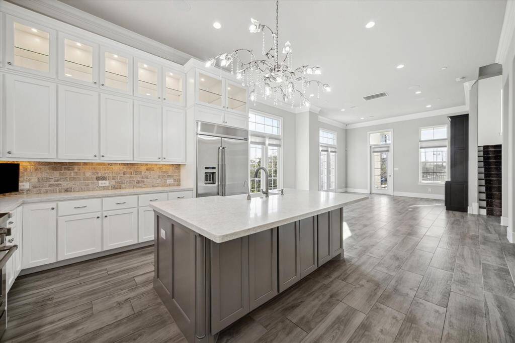This large kitchen view accentuates the soaring ceilings and light filled space.  Enjoy the abundance of cabinets and glass-lit display cabinets for that extra touch.  The brick paver backsplash invites warmth.