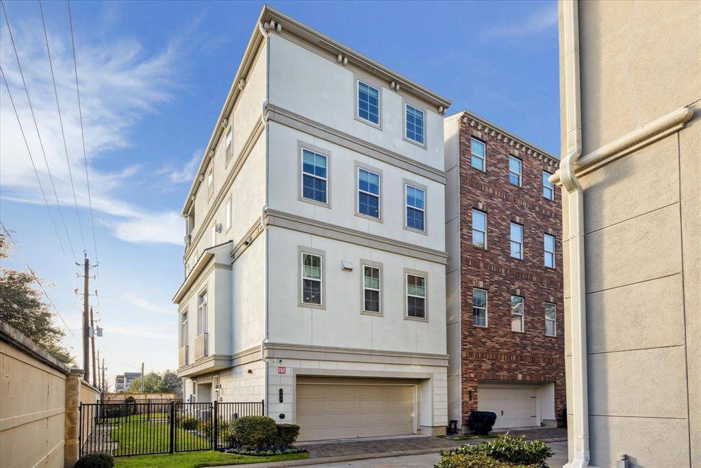 The back of the home, showing the two-car garage access through the alleyway which dead ends at the property.  Gated access to the fenced in yard.  Garage features additional storage and a door to the sideyard.
