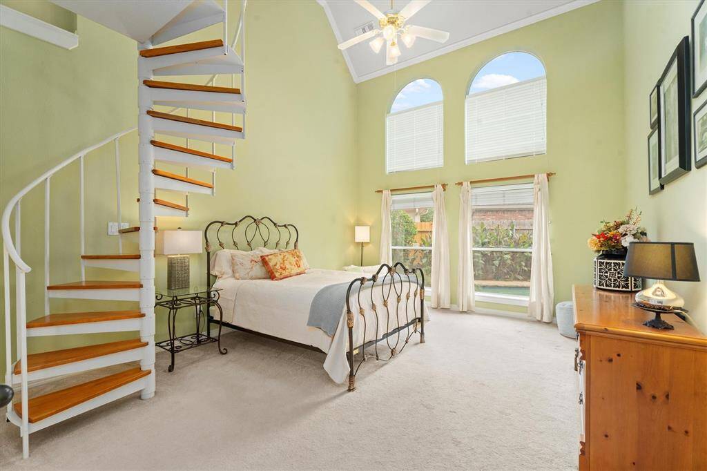 Discover the serene ambiance of this sunlit primary bedroom, featuring grand windows that usher in natural light. A charming spiral staircase beckons you to an exclusive loft space, perfect for a secluded home office or creative retreat.