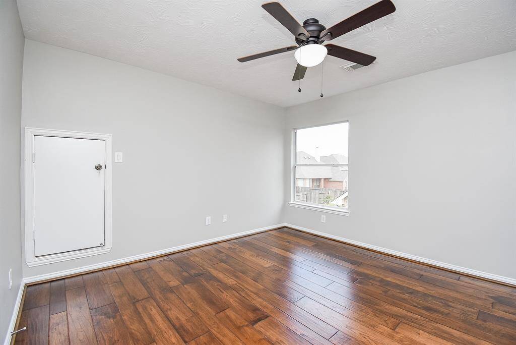 Secondary bedroom featuring rich hardwood flooring, neutral-toned walls, and a large window allowing for ample natural light.
