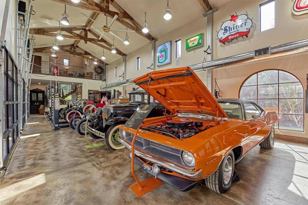 Four of eight climate-controlled bays, highlighting meticulously maintained vintage automobiles, have high vaulted ceiling with exposed wood beams and industrial pendant lighting.