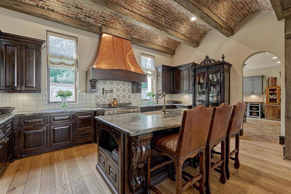 'Fancy kitchen' exudes old-world European elegance with rich wood cabinetry and high-end finishes. Focal point is the striking copper range hood, beautifully complementing the ornate tile backsplash and Bertazzoni gas range.