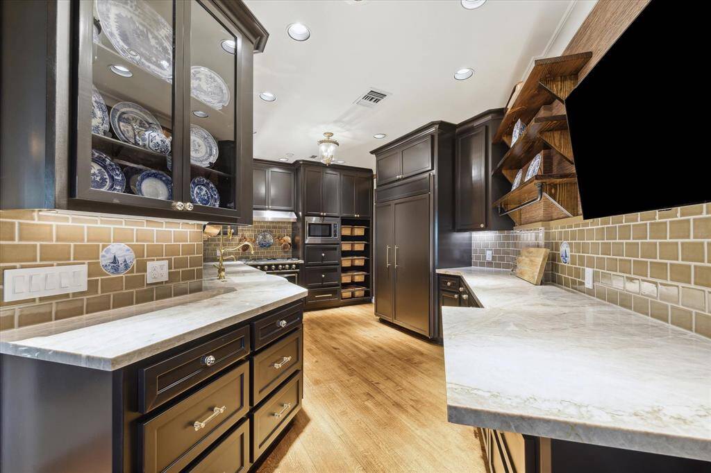 The magazine-worthy kitchen boasts rows of dark, soft-close cabinetry trimmed with MacKenzie-Childs hardware and Taj Mahal quartzite countertops.