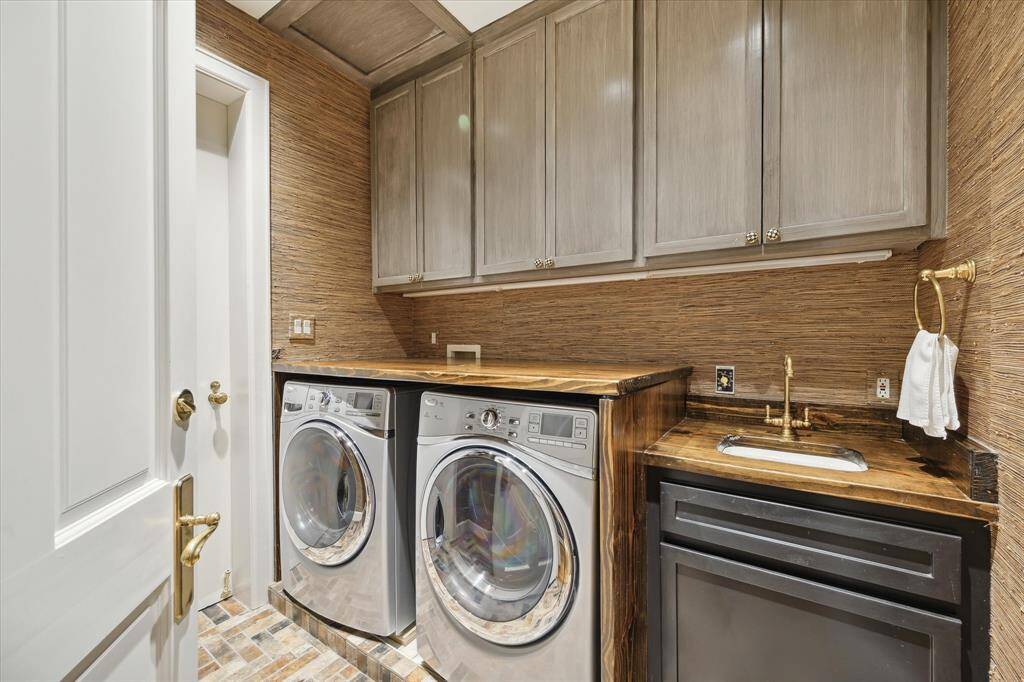 Laundry day is a joy in this spectacular utility room finished with custom cabinetry, a sink, Schumacher grass cloth wallpaper, herringbone tile floors, and access to the service elevators and trash chute.