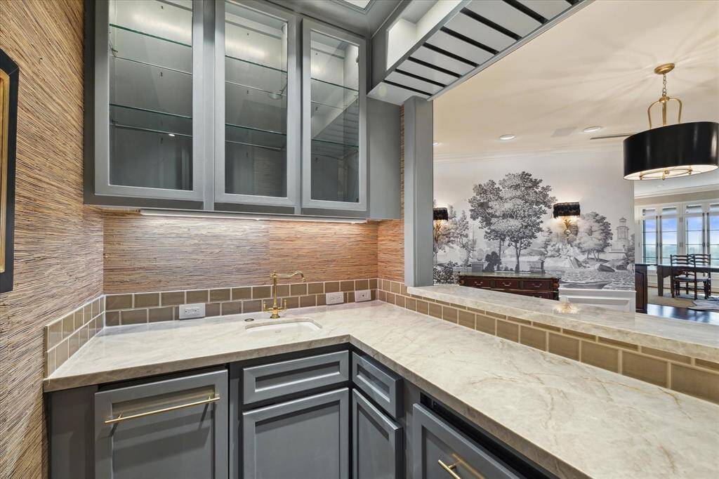 Entertain in style with a beautifully planned walk-up wet bar filled with custom cabinetry, Taj Mahal quartzite, Schumacher grass cloth wallpaper, a wine refrigerator, a Scotsman ice maker and a sink.