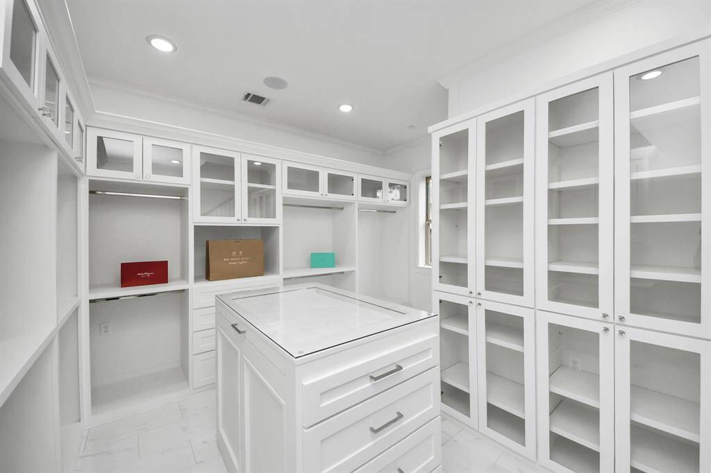 The primary suite offers two custom walk-in closets - this is the 1st floor of one of them, which features surround sound, a glass top island for jewlery storage, glass fronted cabinetry and ample space for hanging items!