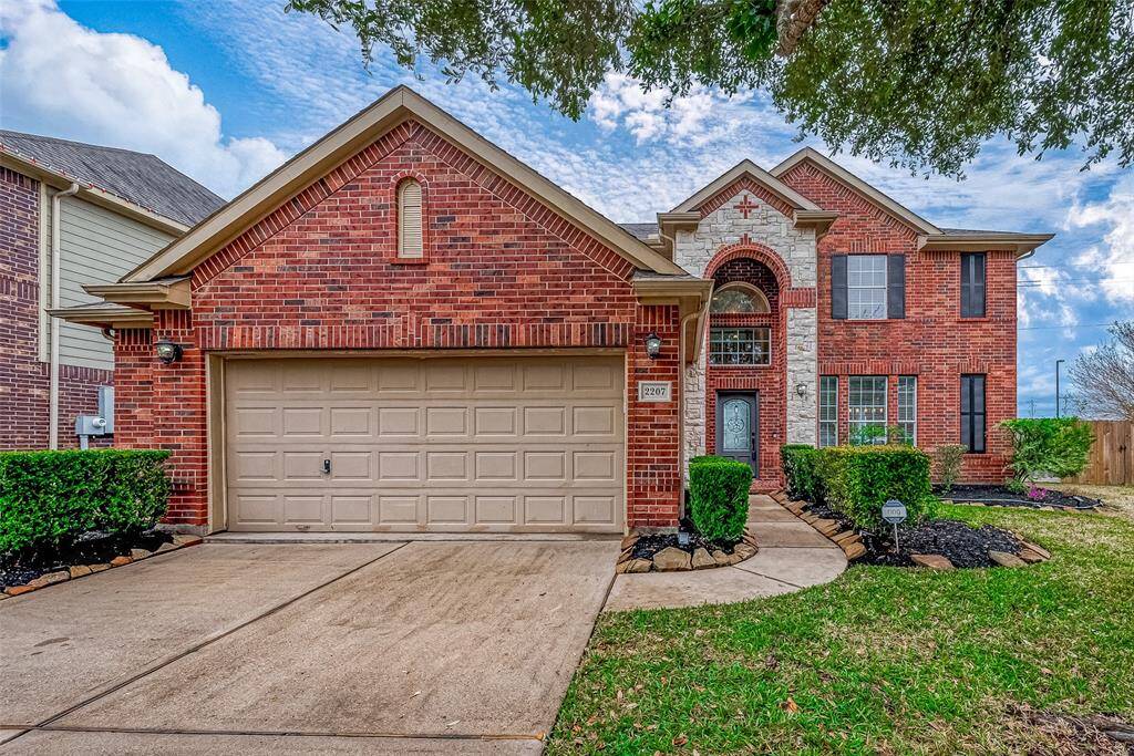 Amazing two-story brick house with an attached two-car garage. It features a well-maintained front yard with hedges and a pathway leading to a decorative front door. The house has a combination of brick and stone accents, adding to its curb appeal.
