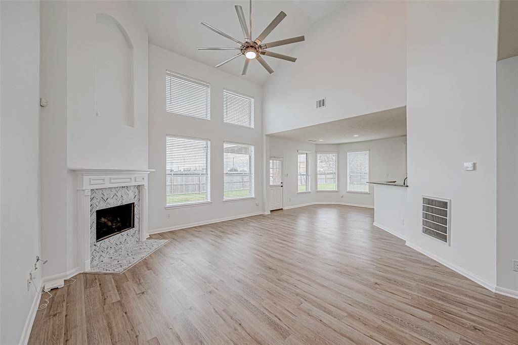 This spacious, bright living area features high ceilings, large windows, and a modern ceiling fan. The room includes a cozy fireplace with a stylish tile surround and transitions into an open dining area with a view of the backyard. Perfect for entertaining and family gatherings.