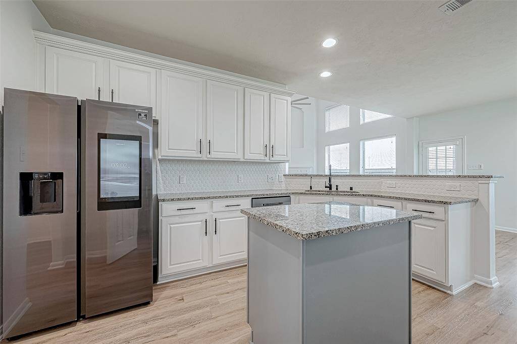 This modern kitchen features sleek stainless steel appliances, white cabinetry, and a spacious granite island. The open layout and large windows provide ample natural light, creating an inviting and functional space.