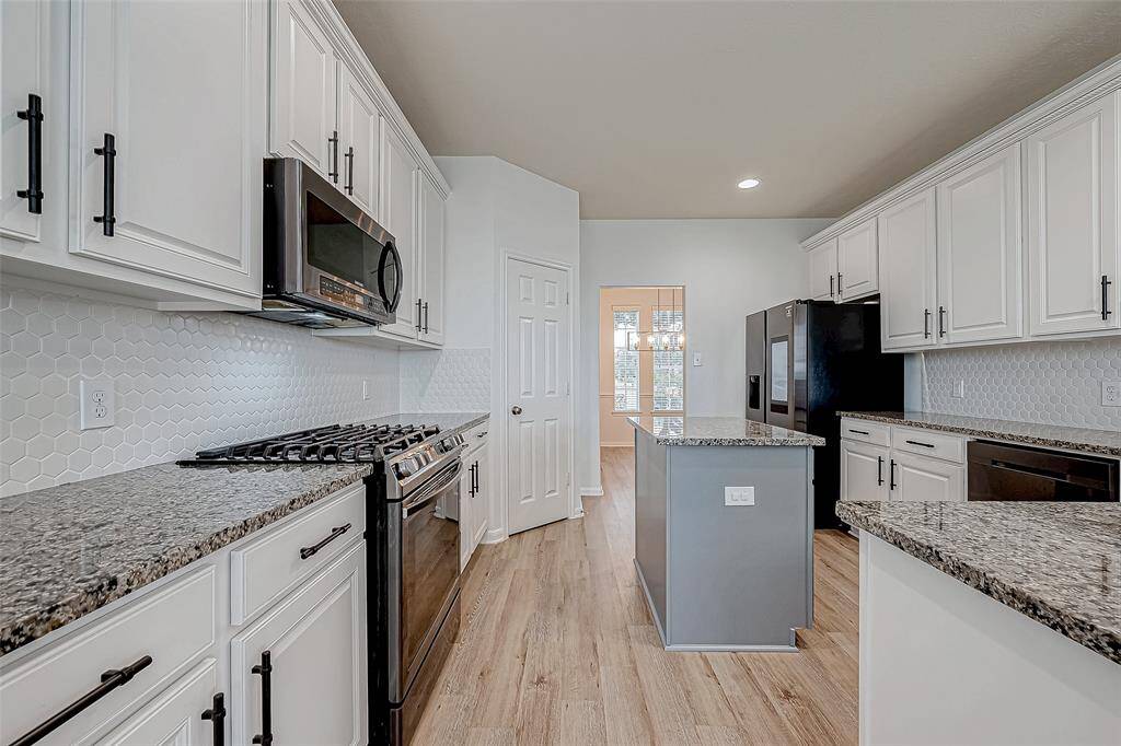 Modern kitchen with granite countertops, white cabinetry, and stainless steel appliances. Features a central island and light wood flooring, creating a bright and inviting space.