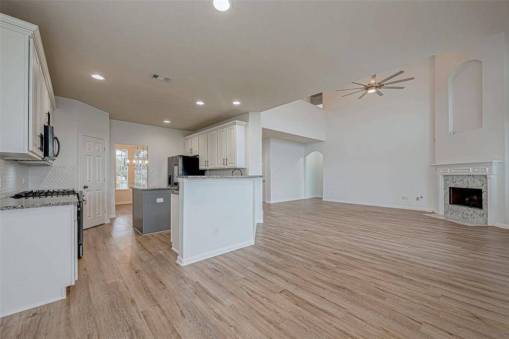 This spacious open-concept living area features a modern kitchen with granite countertops, a cozy fireplace, and high ceilings with recessed lighting. The light wood flooring adds warmth, while large windows bring in natural light. Perfect for entertaining and family gatherings.