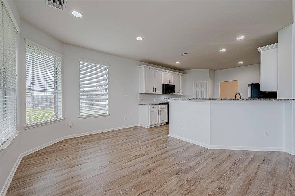 This bright, open-concept kitchen and dining area features modern white cabinetry, granite countertops, and wood-style flooring. Large windows provide ample natural light, creating a warm and inviting space.