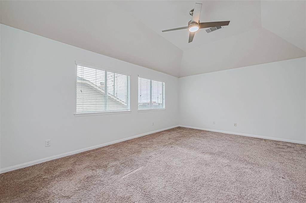 This spacious, carpeted gameroom features a vaulted ceiling with a modern ceiling fan and ample natural light from large windows.