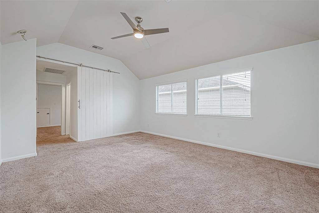 This photo showcases a spacious, gameroom with vaulted ceilings, a ceiling fan, and large windows for natural light. It features a sliding barn door leading to an adjacent area, creating an open and airy feel.