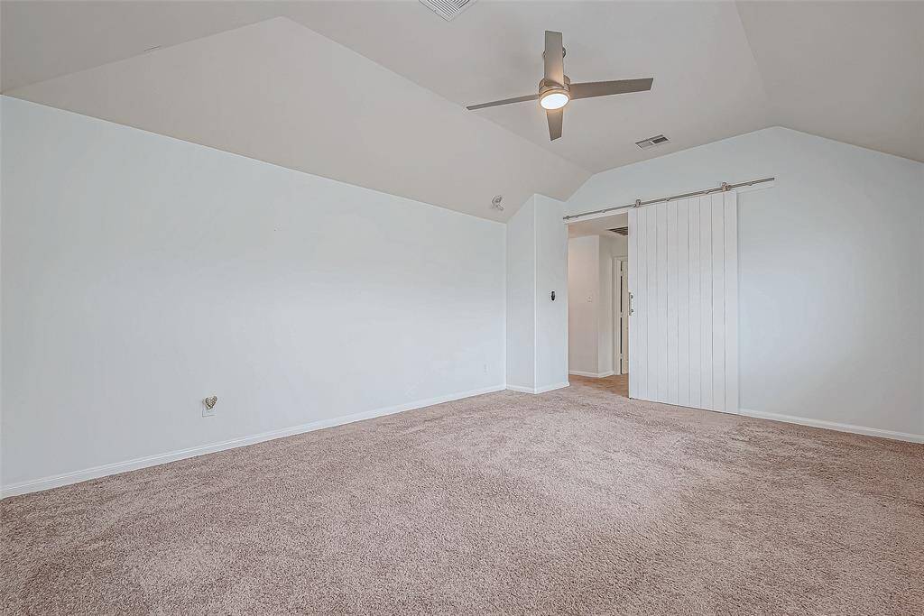 This spacious room features soft carpet flooring, a modern ceiling fan, and a stylish sliding barn door, giving it a cozy and contemporary feel.