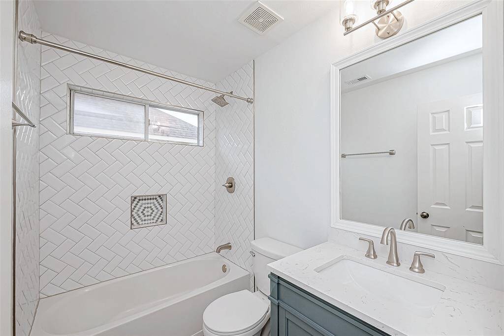 This secondary bathroom features a modern design with a herringbone-tiled shower, built-in niche, and a small window for natural light. It has a sleek vanity with a marble countertop and brushed nickel fixtures, providing a clean and contemporary look.