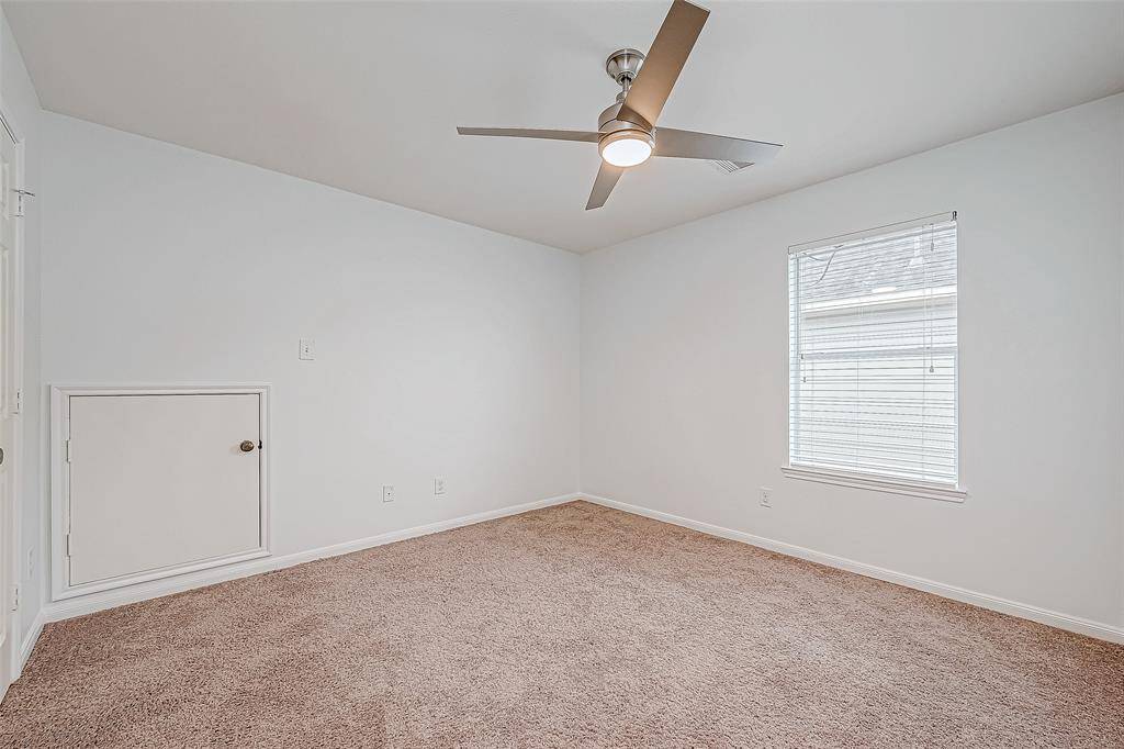 This secondary bedroom features neutral carpeting, a modern ceiling fan, and ample natural light from a single window, creating a cozy and inviting space.