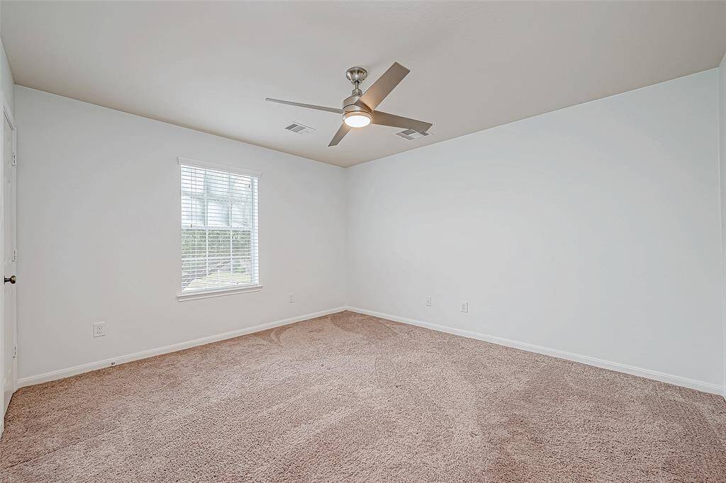 Bright, spacious secondary bedroom with neutral carpet, fresh paint, and a ceiling fan. Ideal for personalization.