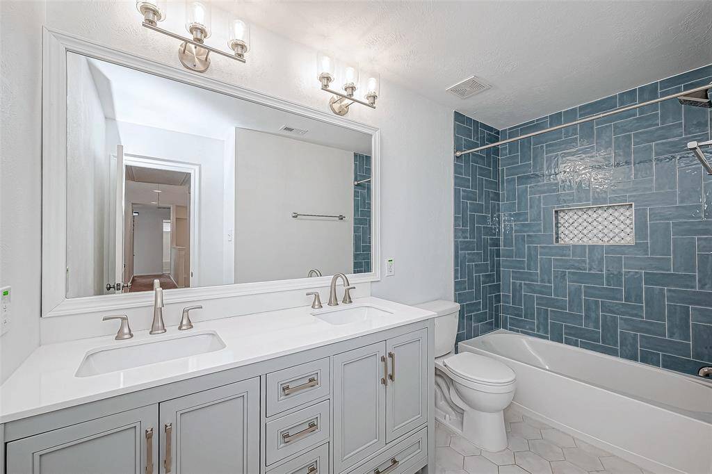 This secondary bathroom features a modern double vanity with sleek fixtures, a large mirror, and elegant lighting. The shower area boasts stylish blue herringbone tiles, adding a touch of sophistication.