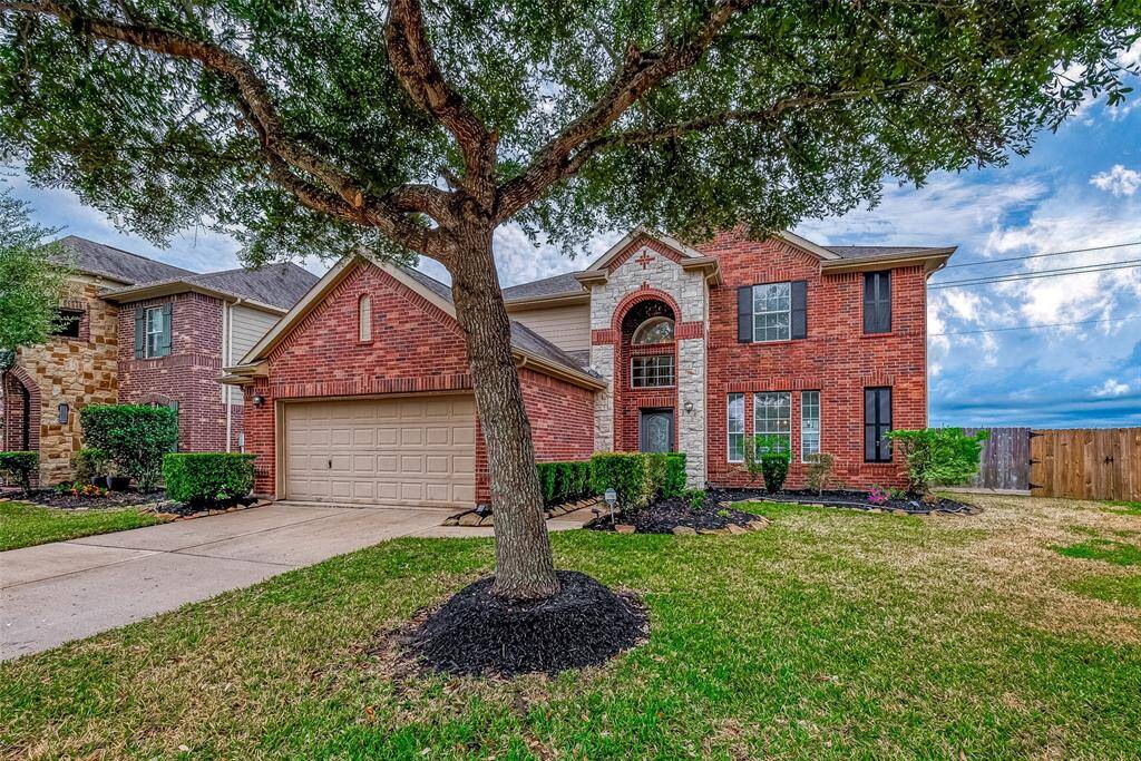 This inviting two-story brick home features a spacious driveway, two-car garage, and charming front landscaping. A mature tree provides shade in the front yard, adding to the curb appeal.