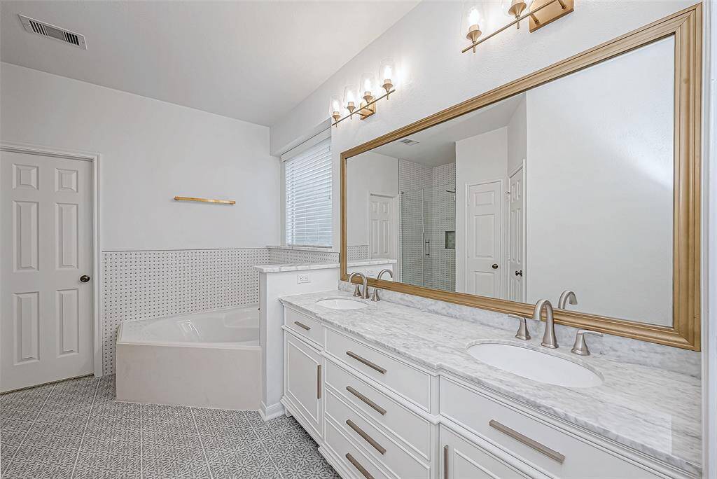 The primary bath features a spacious layout with a large double vanity and marble countertops, elegant fixtures, a soaking tub, and a separate shower. The neutral tones and ample lighting create a bright and modern atmosphere.