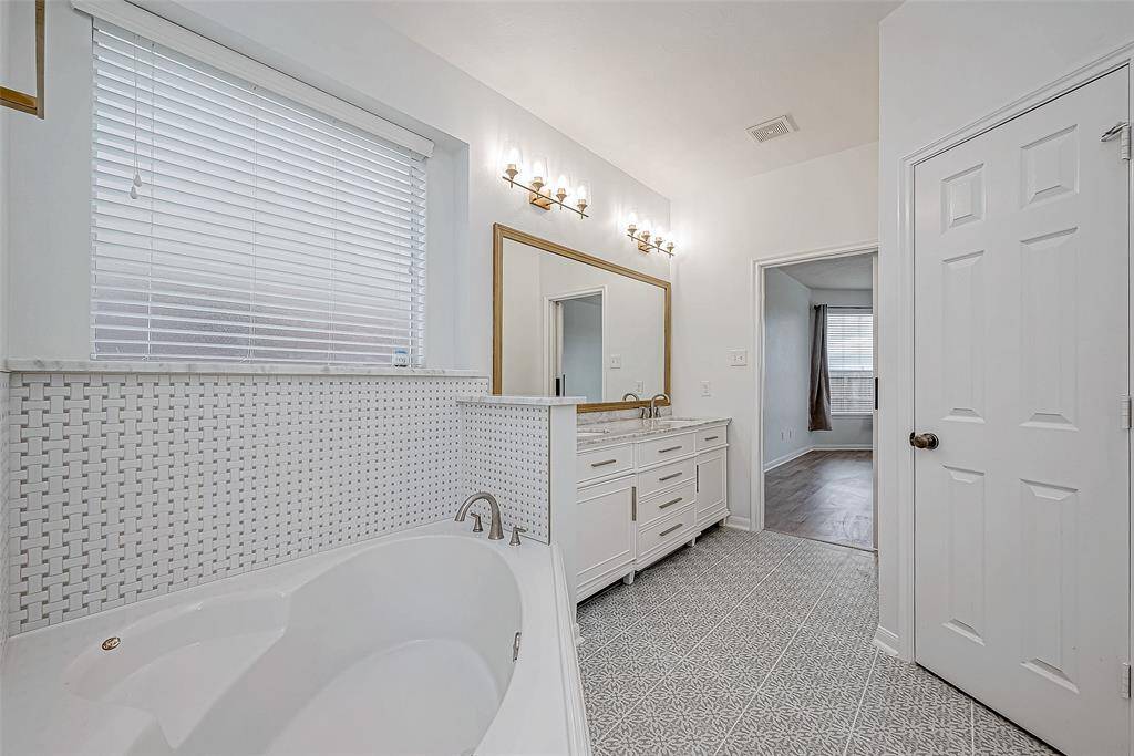 The primary bathroom features a modern design with a spacious vanity, elegant lighting, and a large soaking tub. The patterned floor tiles and textured wall tiles add a touch of sophistication.