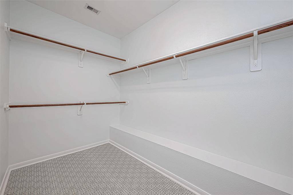 Spacious walk-in closet in the primary bedroom with multiple wooden hanging rods and a patterned floor. The white walls and ceiling create a bright, clean atmosphere.