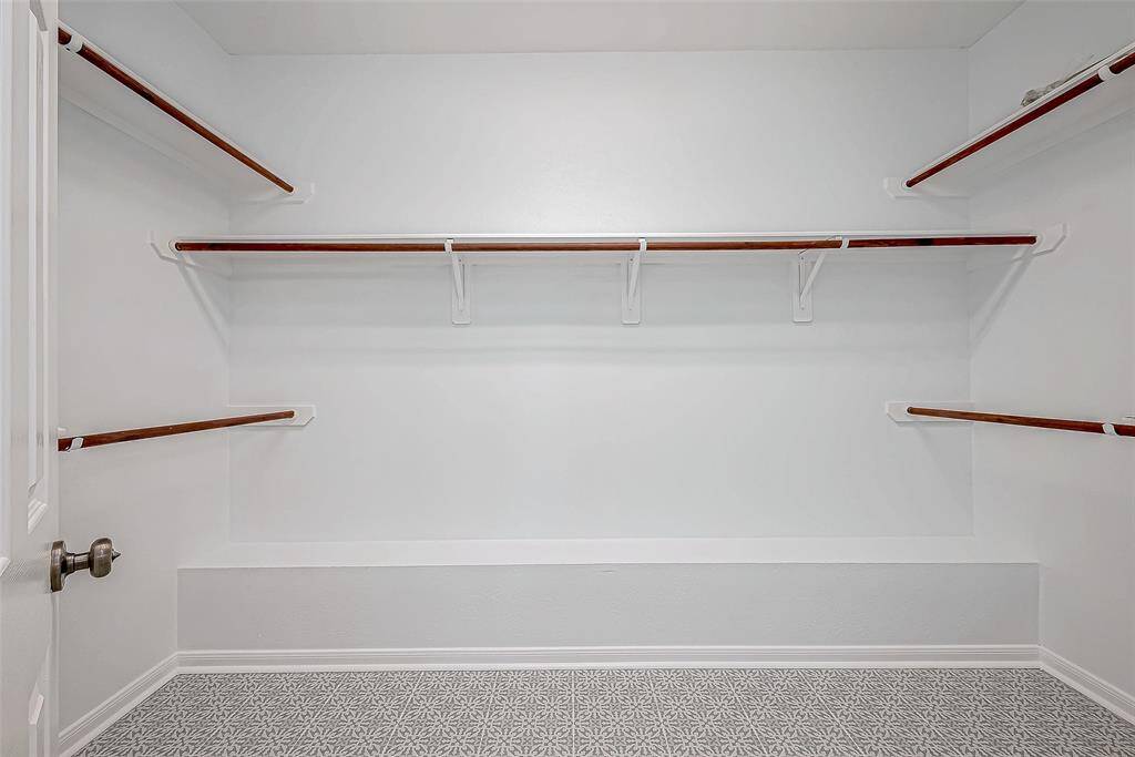 Spacious walk-in closet with multiple wooden shelves and a patterned floor, offering ample storage and organization space.