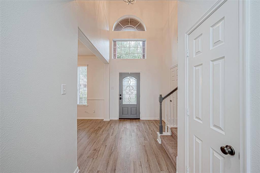 Bright entryway with high ceilings, large windows, and stylish luxury wood vinyl flooring. Features a decorative front door and a staircase with modern railing.
