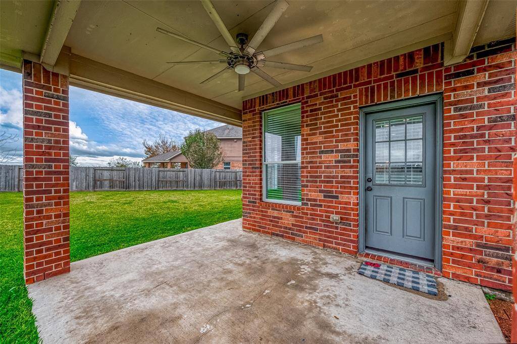 This photo showcases a covered patio with a ceiling fan, featuring a brick exterior and adjacent to a spacious, fenced backyard—ideal for outdoor relaxation and entertainment.