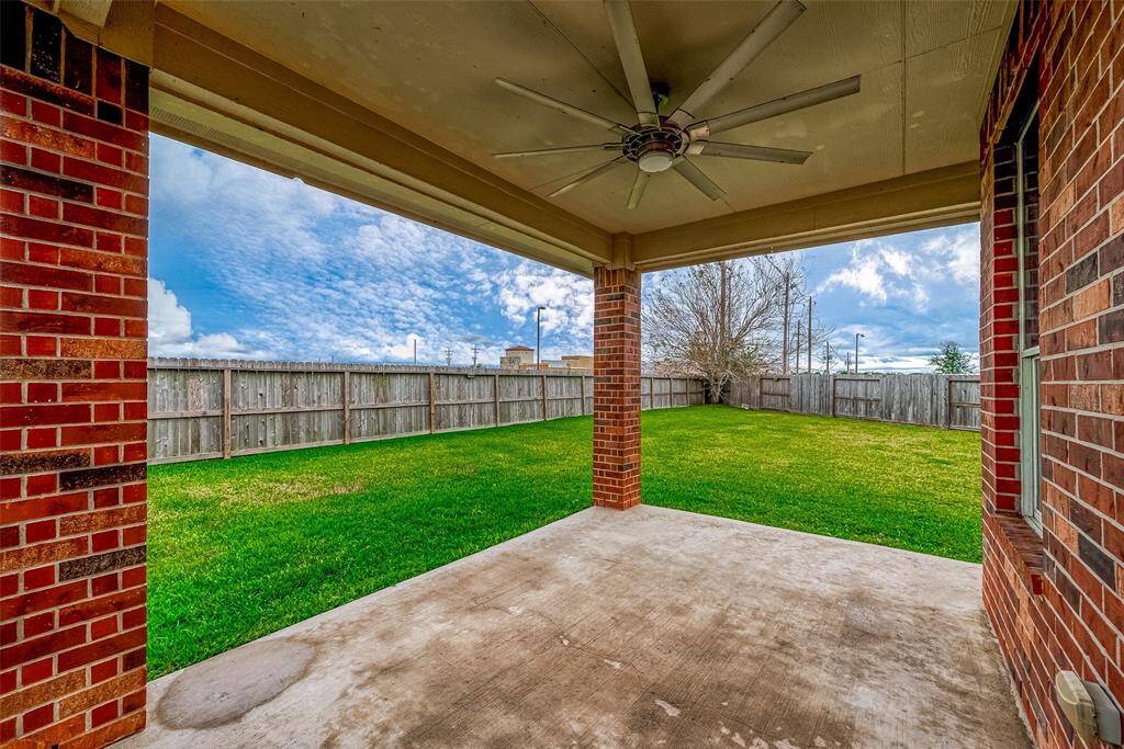 This photo showcases a spacious covered patio with a ceiling fan, overlooking a large, fenced backyard with lush green grass, perfect for outdoor relaxation and entertainment.