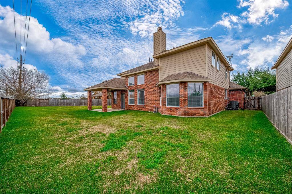 This photo showcases a spacious backyard with a well-maintained lawn, a two-story brick home with a chimney, and a covered patio. The property is fenced, providing privacy and ample outdoor space.