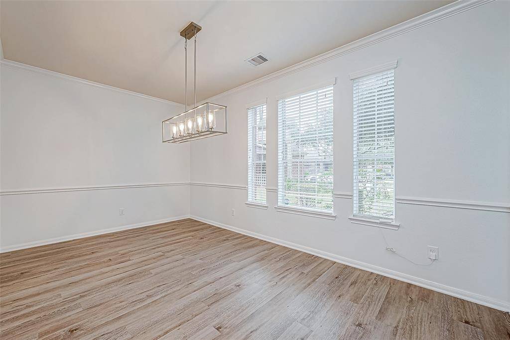 This room features a modern chandelier, large windows with blinds, and light wood flooring, creating a bright and inviting space. Perfect for dining or a versatile living area.