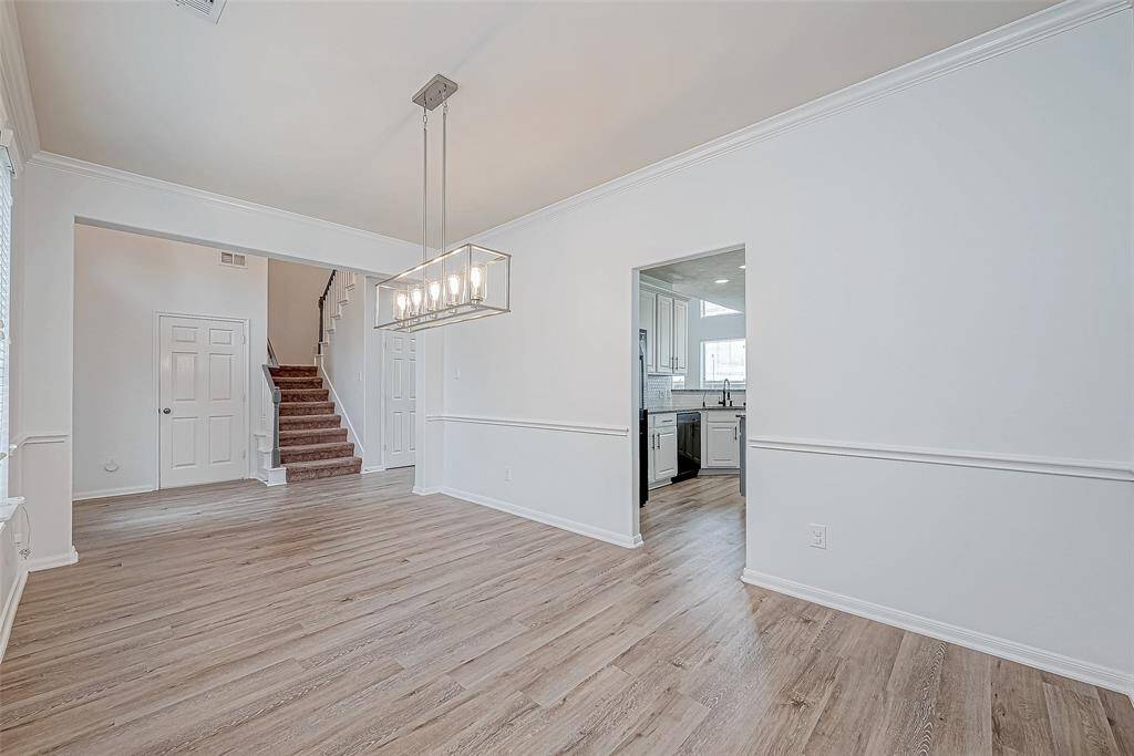 Bright dining area with wood flooring, modern light fixture, and neutral walls. Open access to the kitchen and nearby carpeted staircase. Ideal for entertaining and family gatherings.