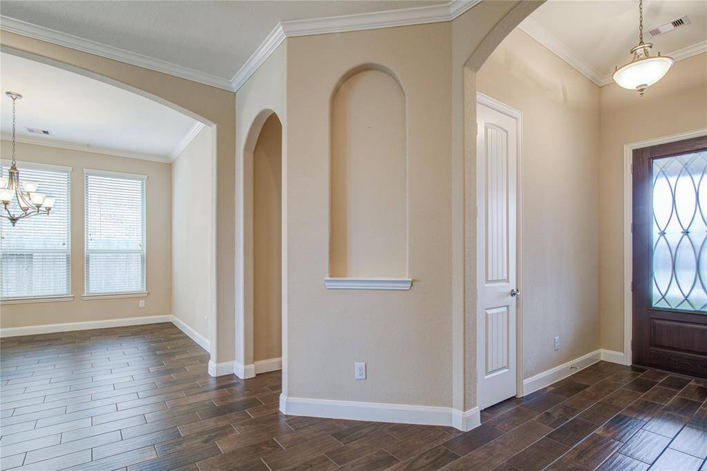 Wood-look tile flooring, tall ceilings and crown molding create an elegant feel in the home. The archway to the right of the dining room leads to the mud bench, utility room, and garage.