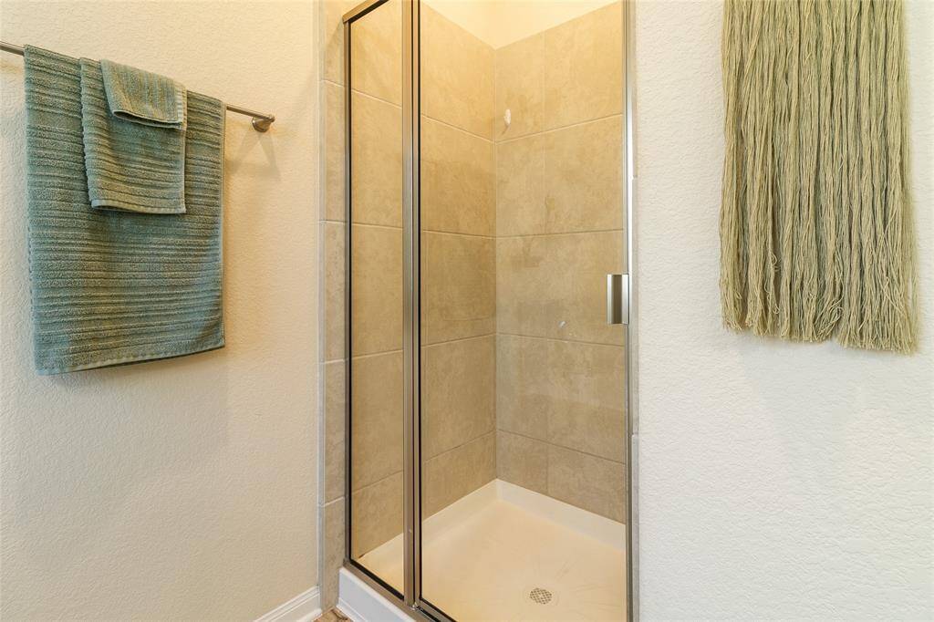 Step into the separate shower of the primary bathroom, featuring stylish tiled walls & a frameless glass door that adds a sleek, modern touch to the space.