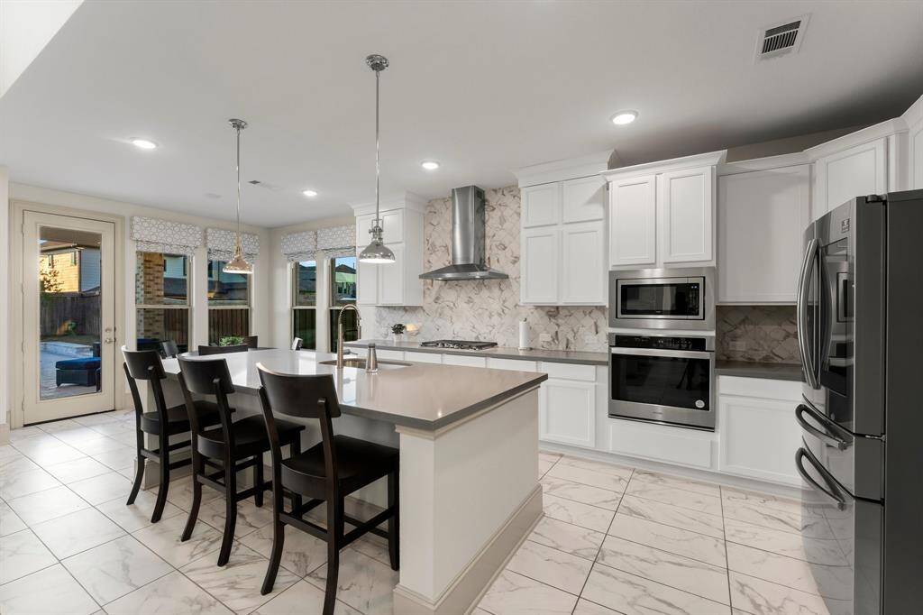 Kitchen wows with stainless steel appliances, and a central island with seating. Large windows and a glass door offer natural light and a view of the pool.