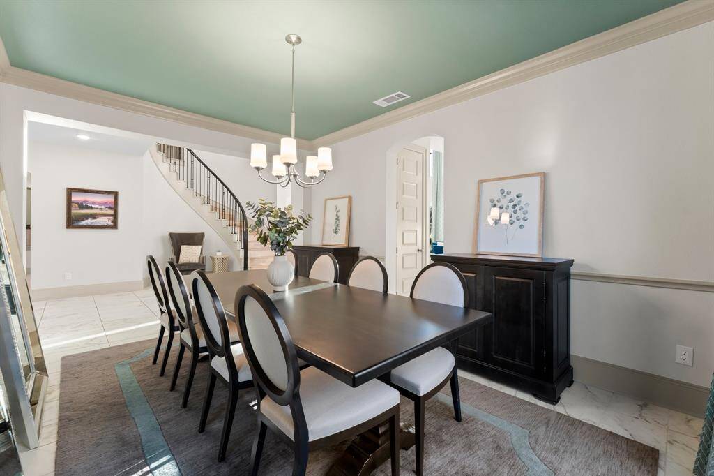 Elegant dining room with a modern chandelier and accent paint. Nearby is a staircase with a sleek railings that add architectural interest.