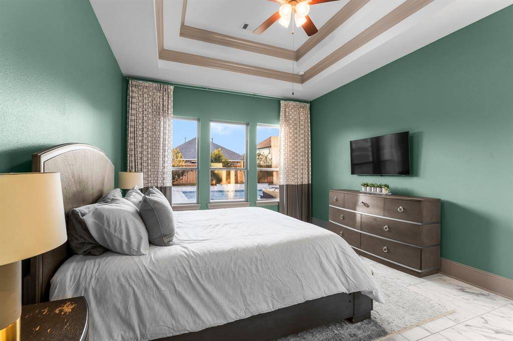 Primary bedroom boasts a stunning tray ceiling and sleek tile floors.