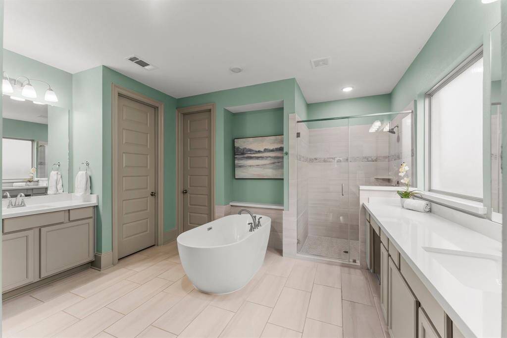 Primary bathroom features a freestanding bathtub, a large walk-in shower with glass doors, dual vanities, and ample natural light.