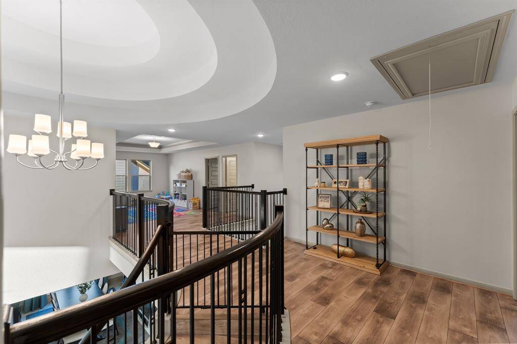 Upstairs area with updated LVT flooring and a stylish black railing. A chandelier illuminates the space, which includes a play area.