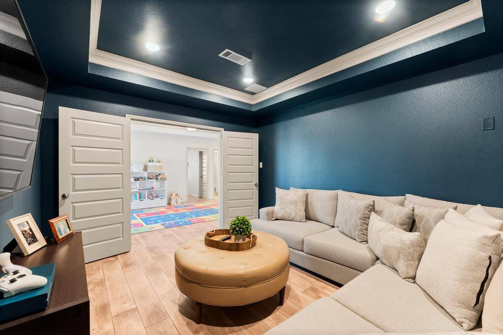 Cozy media room with deep blue walls and recessed lighting. Double doors open to the playroom, adding versatility to the space.