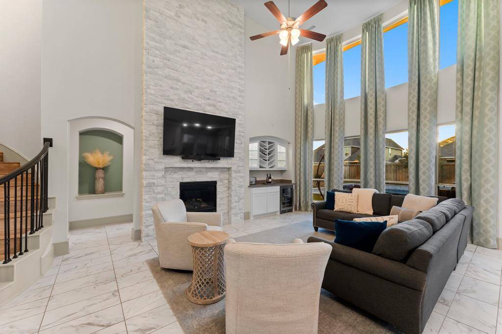 This living room features an upgraded stone, gas fireplace, high ceilings with large windows, and elegant drapery.