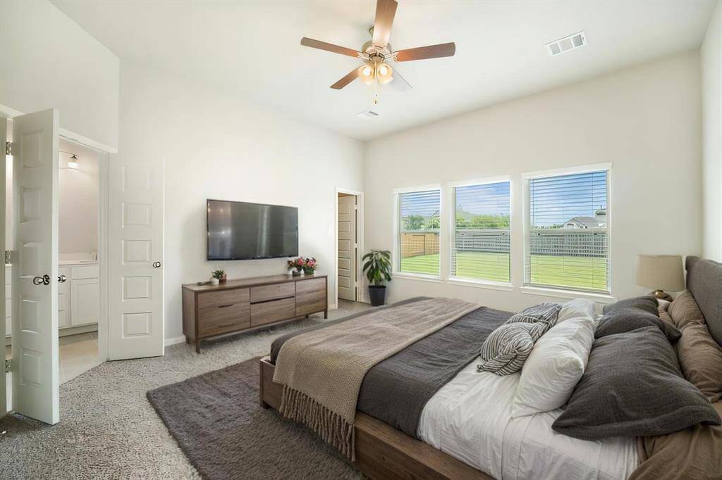 This bright and airy primary suite offers ample space for relaxation, with easy access to the ensuite bath and dual walk-in closets. The neutral color palette and large windows make it the perfect canvas to personalize. Enjoy the ceiling fan and plush carpeting, creating a cozy yet sophisticated atmosphere.
