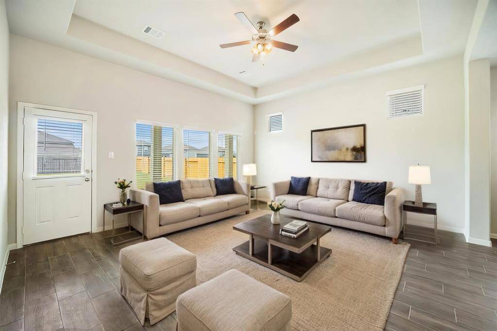 Bask in the warmth of natural light in this expansive living area featuring tray ceilings, a ceiling fan, and wide-format ceramic tile flooring. The large windows invite the outdoors in, offering a seamless transition to the covered patio and backyard. Whether you’re entertaining guests or enjoying a quiet evening, this open and airy space provides the perfect setting for modern living.