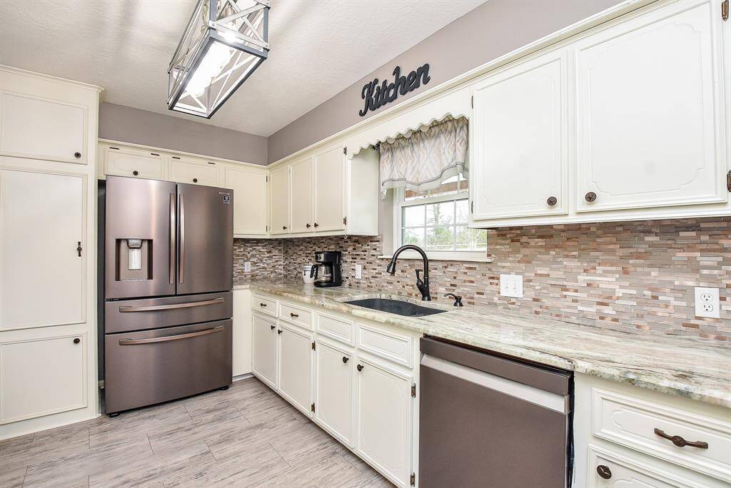 A welcomed window above the farm house style sink is complemented by lush counter space, cabinetry and drawers below, appealing mosaic-like tile backsplash, and hefty stainless steel appliances, adding to the quiet glow of this special space.